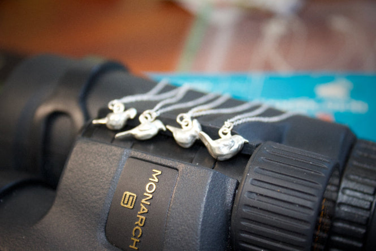 4 sterling silver bird charms on necklaces on a pair of binoculars with a blurred background