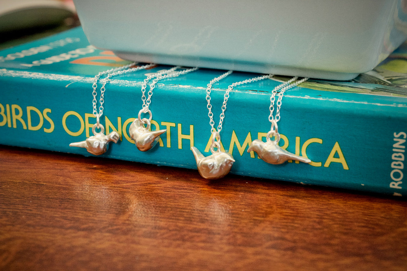 four sterling silver bird charms on chains on a book titled 'Birds of North America'.