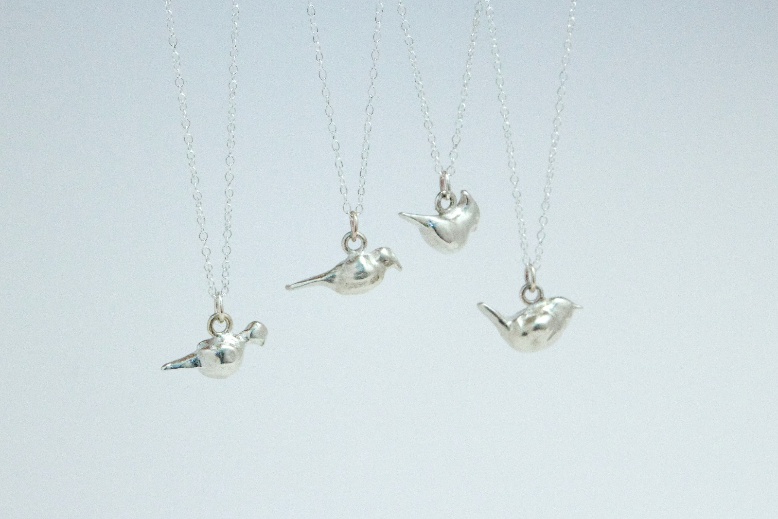 four sterling silver bird charms, a mourning dove, a crow, a cardinal, and a wren.