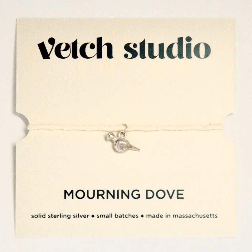 Silver 'Mourning Dove' charm on a Vetch Studio card with product details.