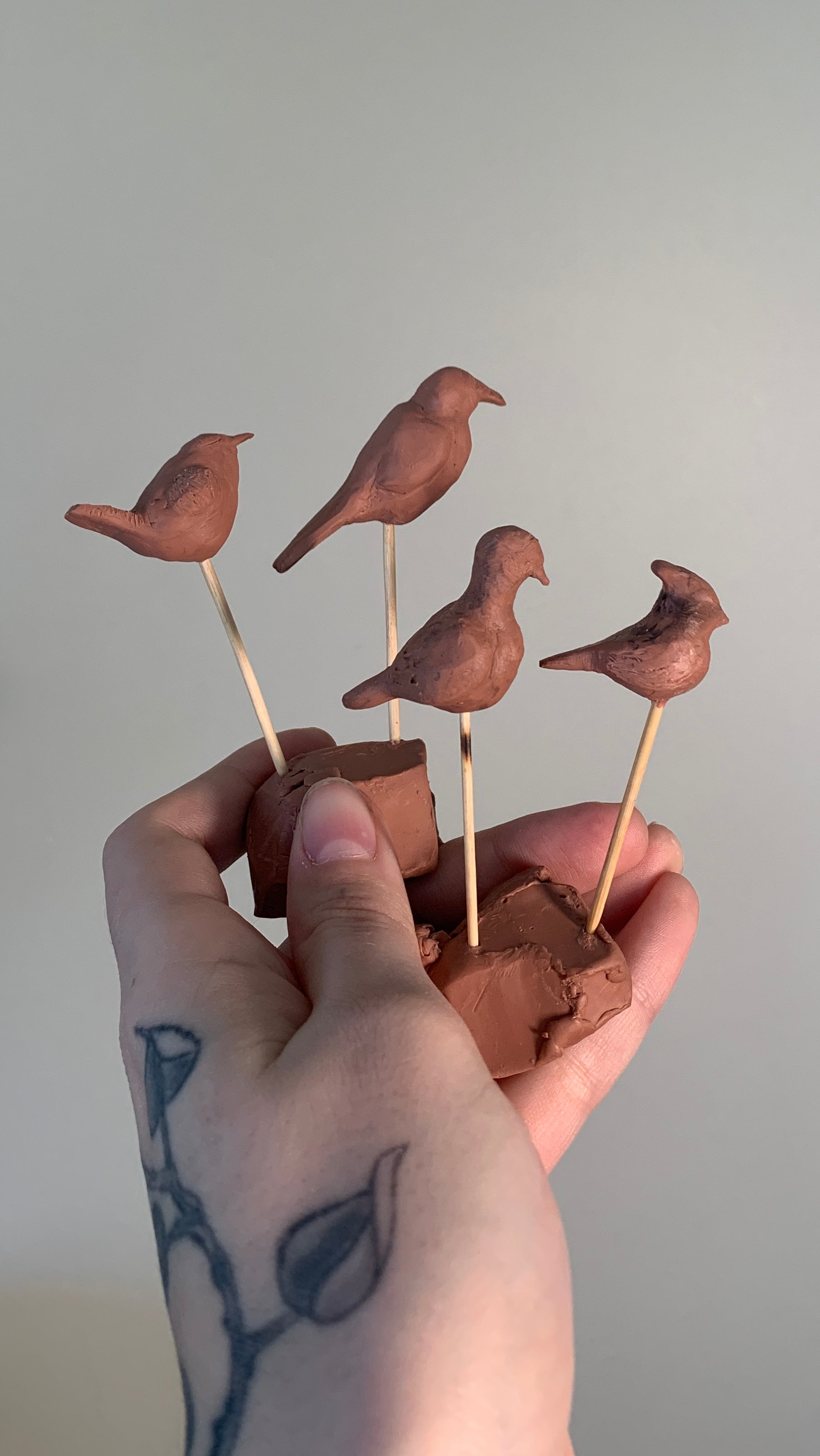 a hand holding 4 small clay sculptures of birds created during the process of designing the vetch studio jewelry.