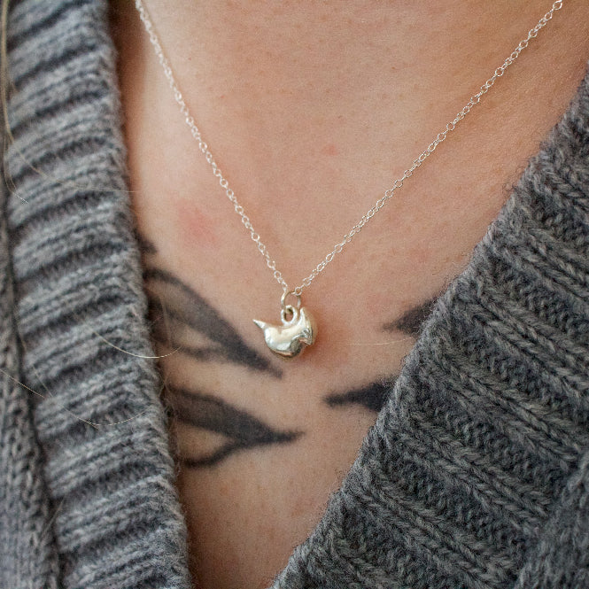 sterling silver cardinal charm on a necklace worn by a model in a grey sweater.