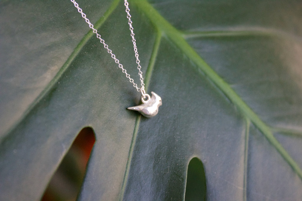 a product image of a sterling silver cardinal charm in front of a plant