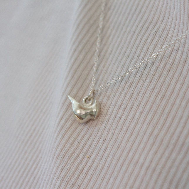 a sterling silver cardinal bird charm on a chain in front of a white shirt.