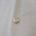 a sterling silver cardinal bird charm on a chain in front of a white shirt.