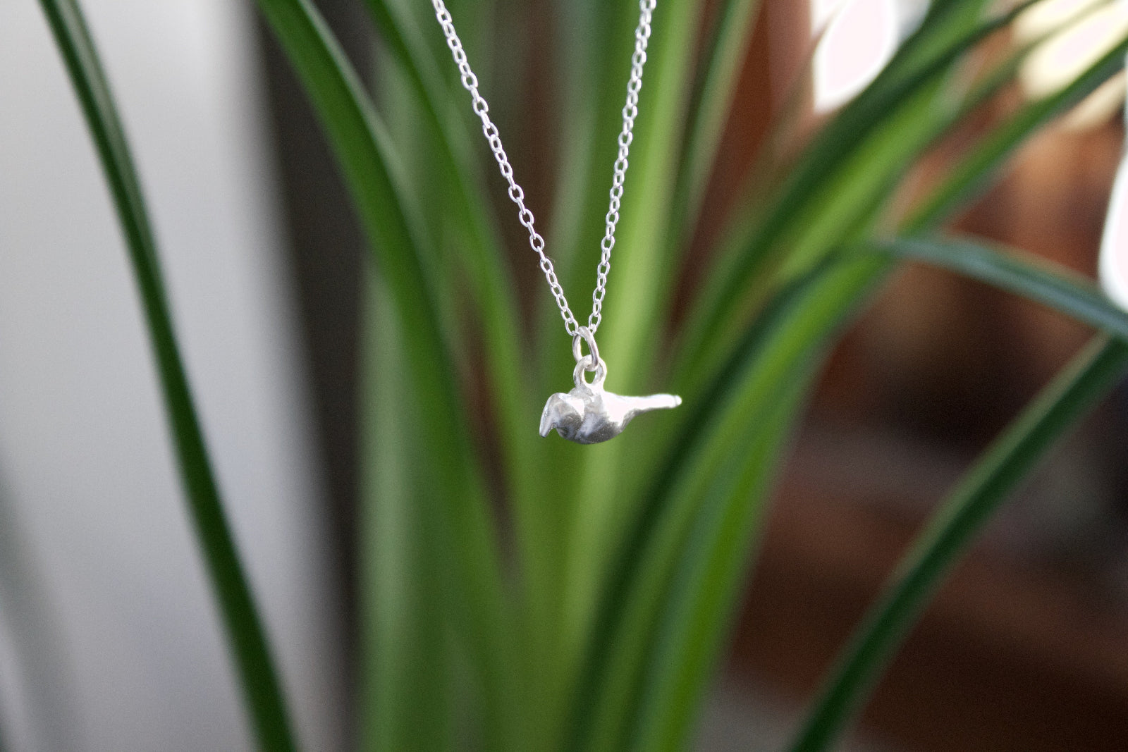 a product image of a sterling silver crow charm in front of a plant