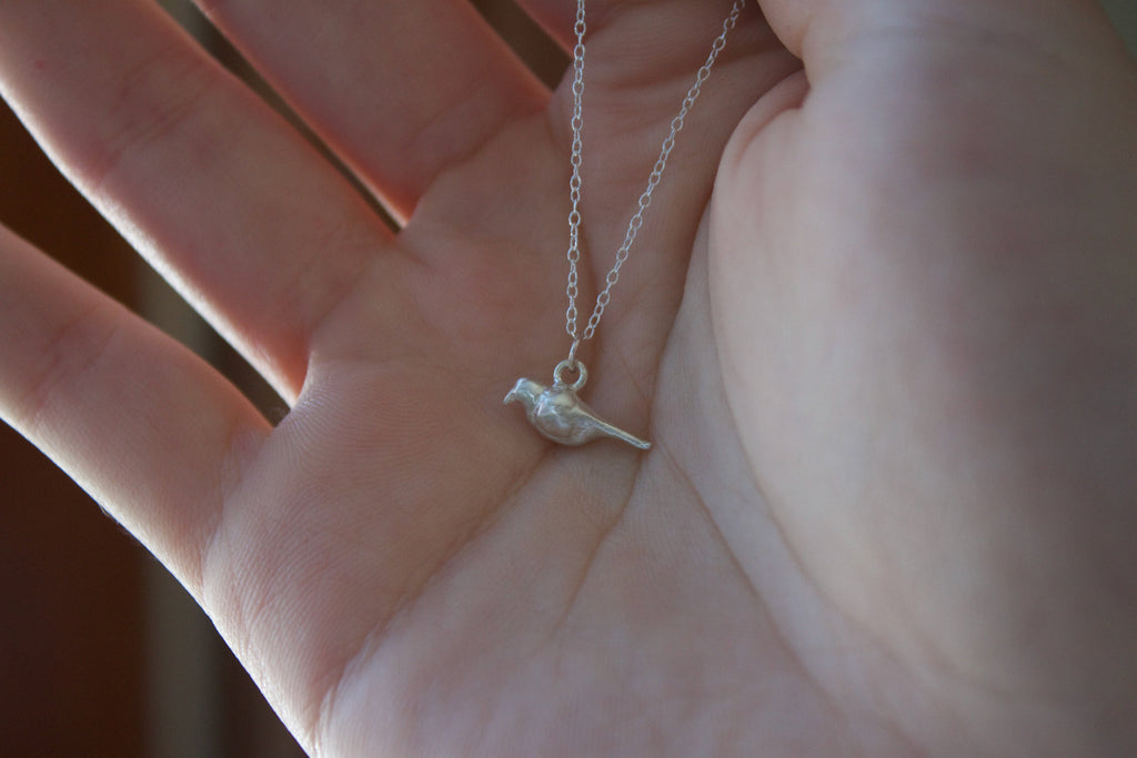 a sterling silver crow charm on a chain necklace held in a hand