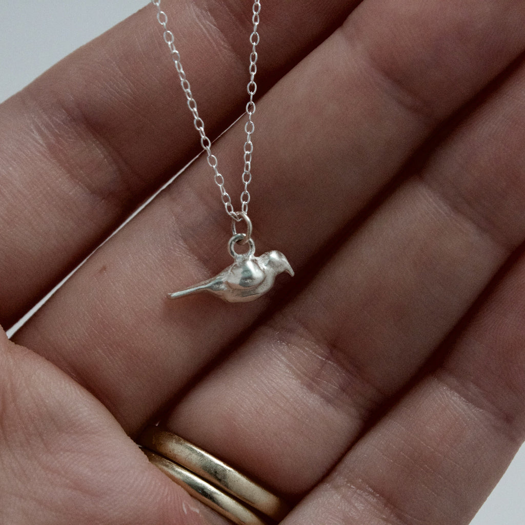 Silver bird necklace on a hand