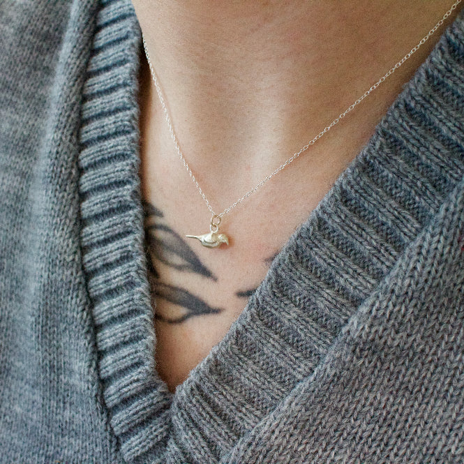 Sterling silver necklace with a small crow pendant worn by a person in a gray sweater.