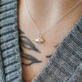 Sterling silver necklace with a small crow pendant worn by a person in a gray sweater.