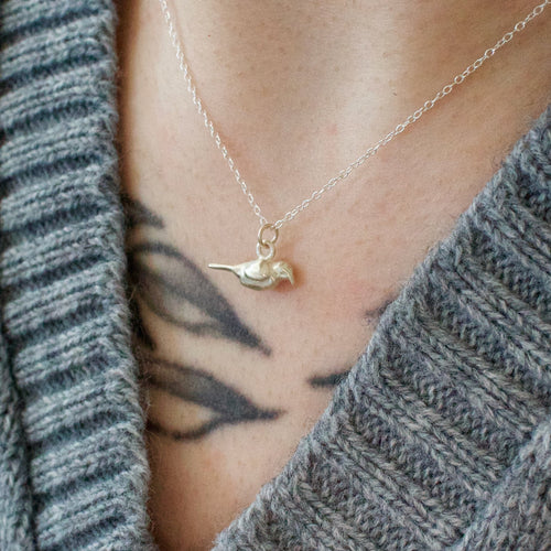 Sterling silver necklace with a small crow pendant worn by a person in a gray sweater.