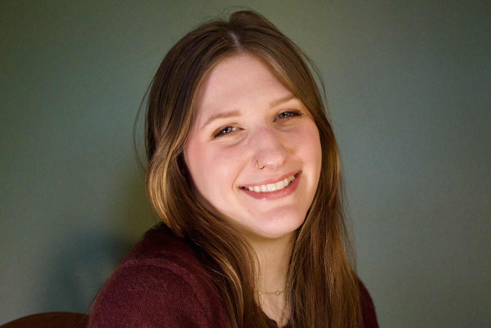 Woman with long brown hair smiling against a plain background