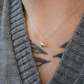 a sterling silver mourning dove pendant worn on a necklace by a person in a grey sweater.