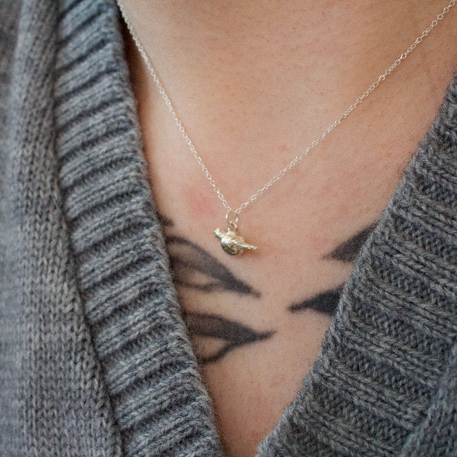 a sterling silver mourning dove pendant worn on a necklace by a person in a grey sweater.