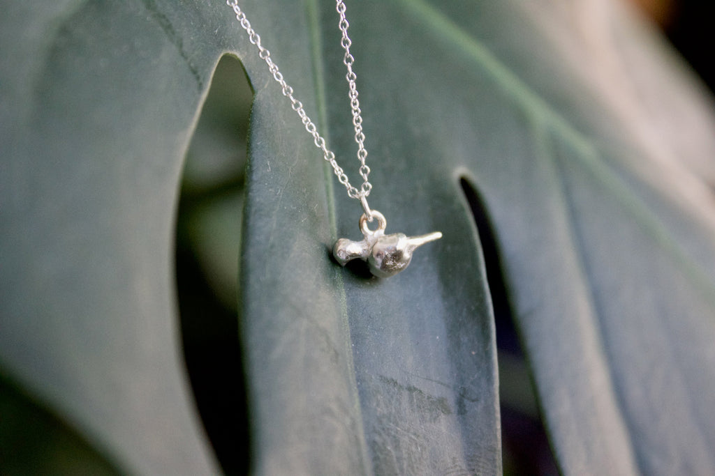 a product image of a sterling silver mourning dove charm in front of a plant