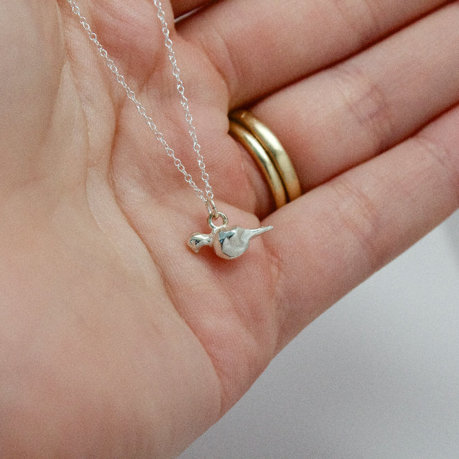 sterling silver mourning dove pendant held in a hand by a chain necklace