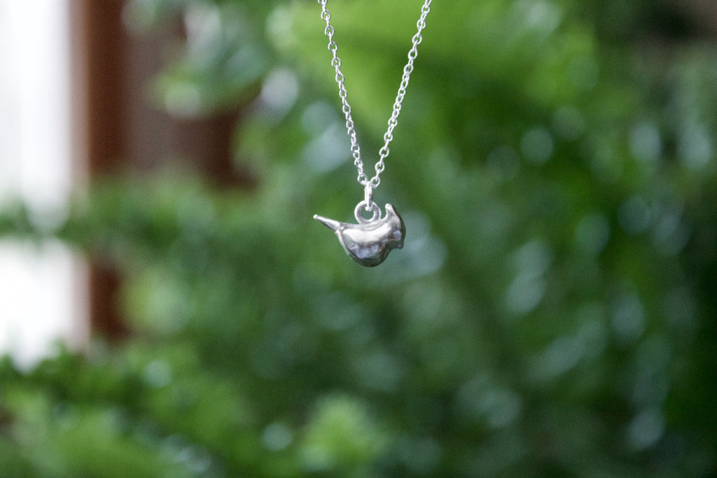 a product image of a sterling silver cardinal charm in front of a plant
