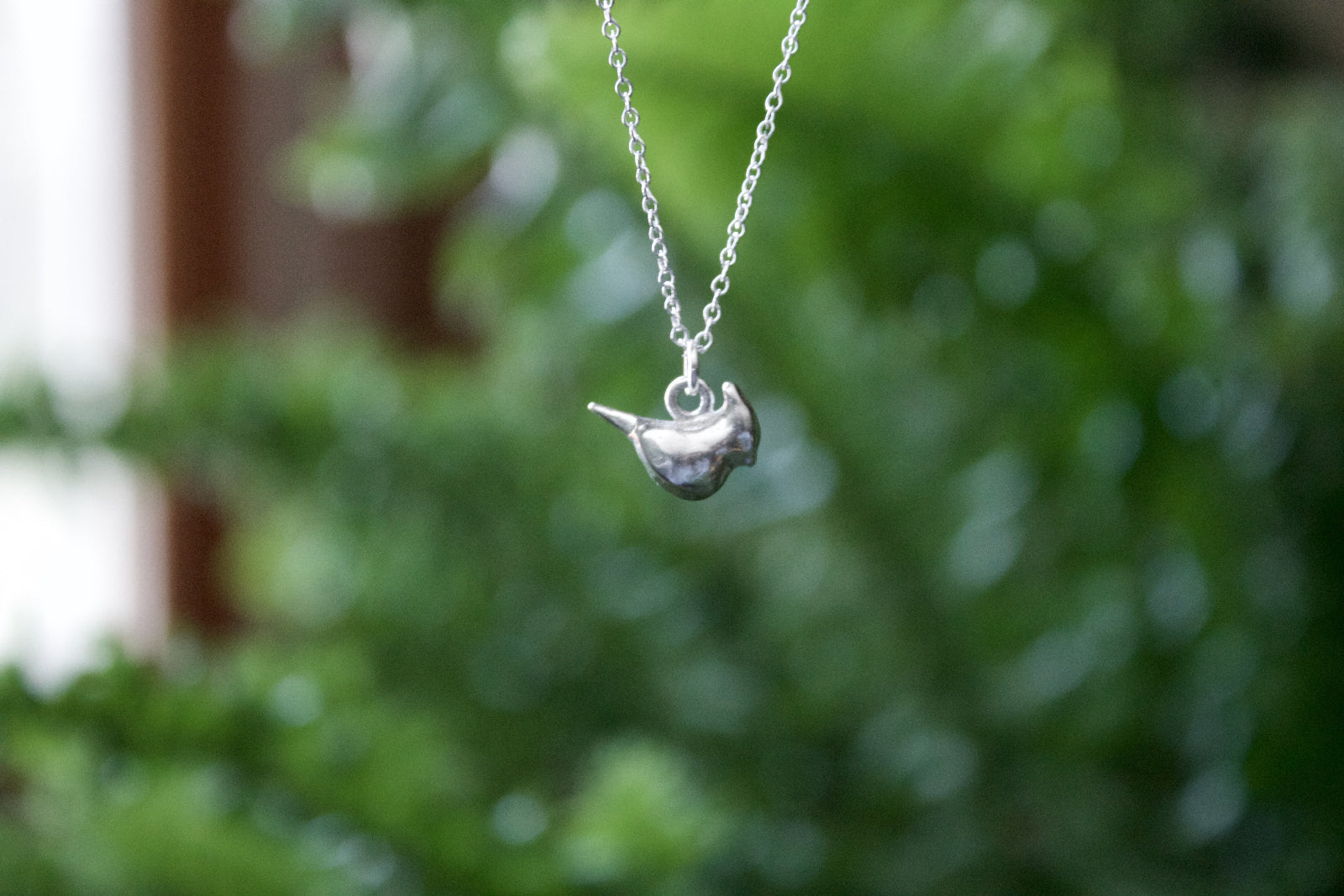 a product image of a sterling silver cardinal charm in front of a plant