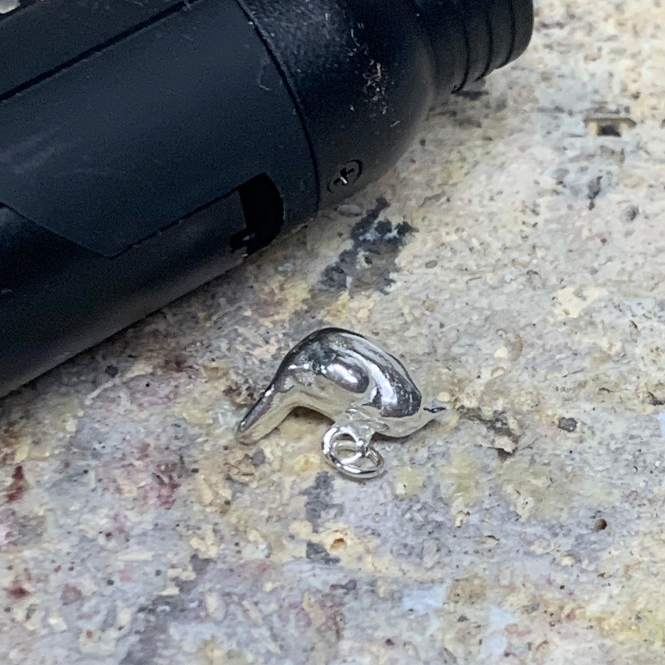 a sterling silver carolina wren charm on a soldering block in a jewelry workshop next to a soldering torch
