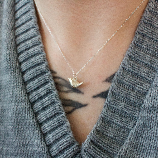 Sterling silver necklace with a small wren pendant worn by a person in a gray sweater.